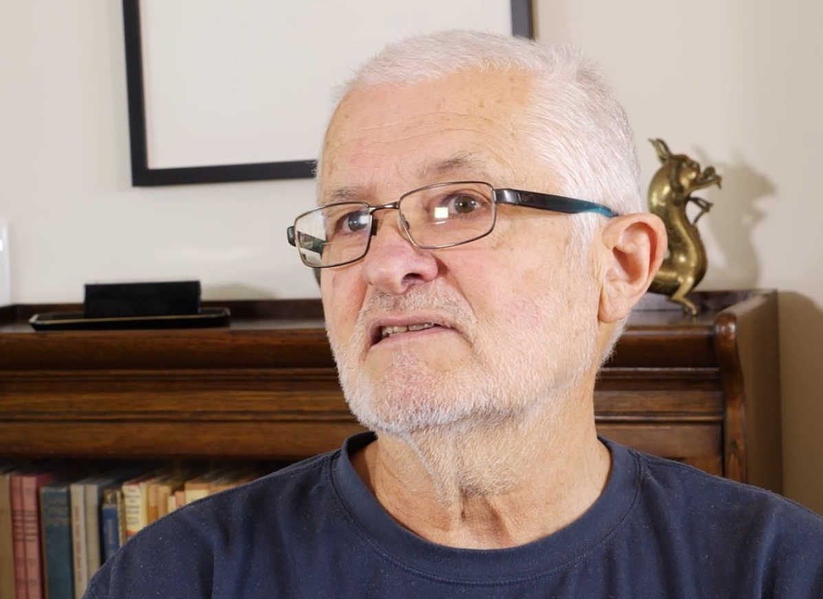 A photo of Peter (informal mentor of The Growing Space). Peter wears glasses, and sits in front of a bright wall and bookcase.